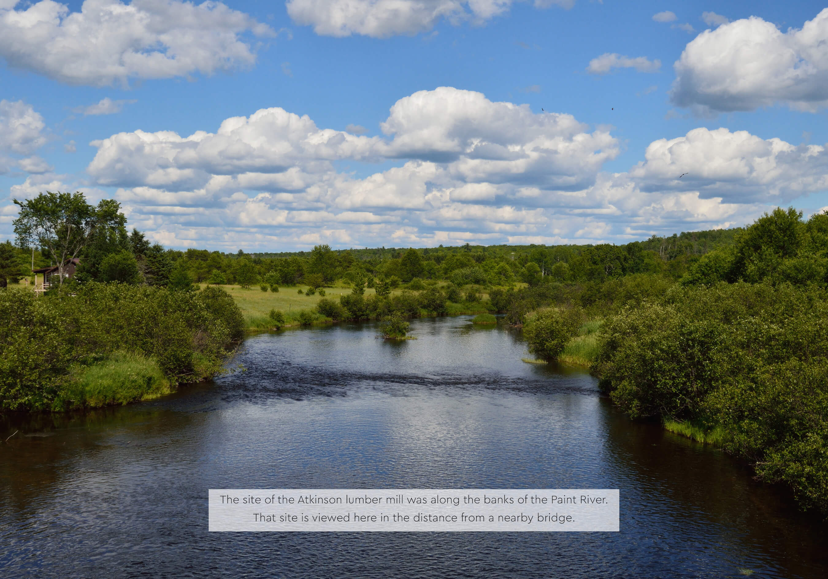 A river with reflective blue water flows between green shrubs and trees under a partly cloudy sky.
