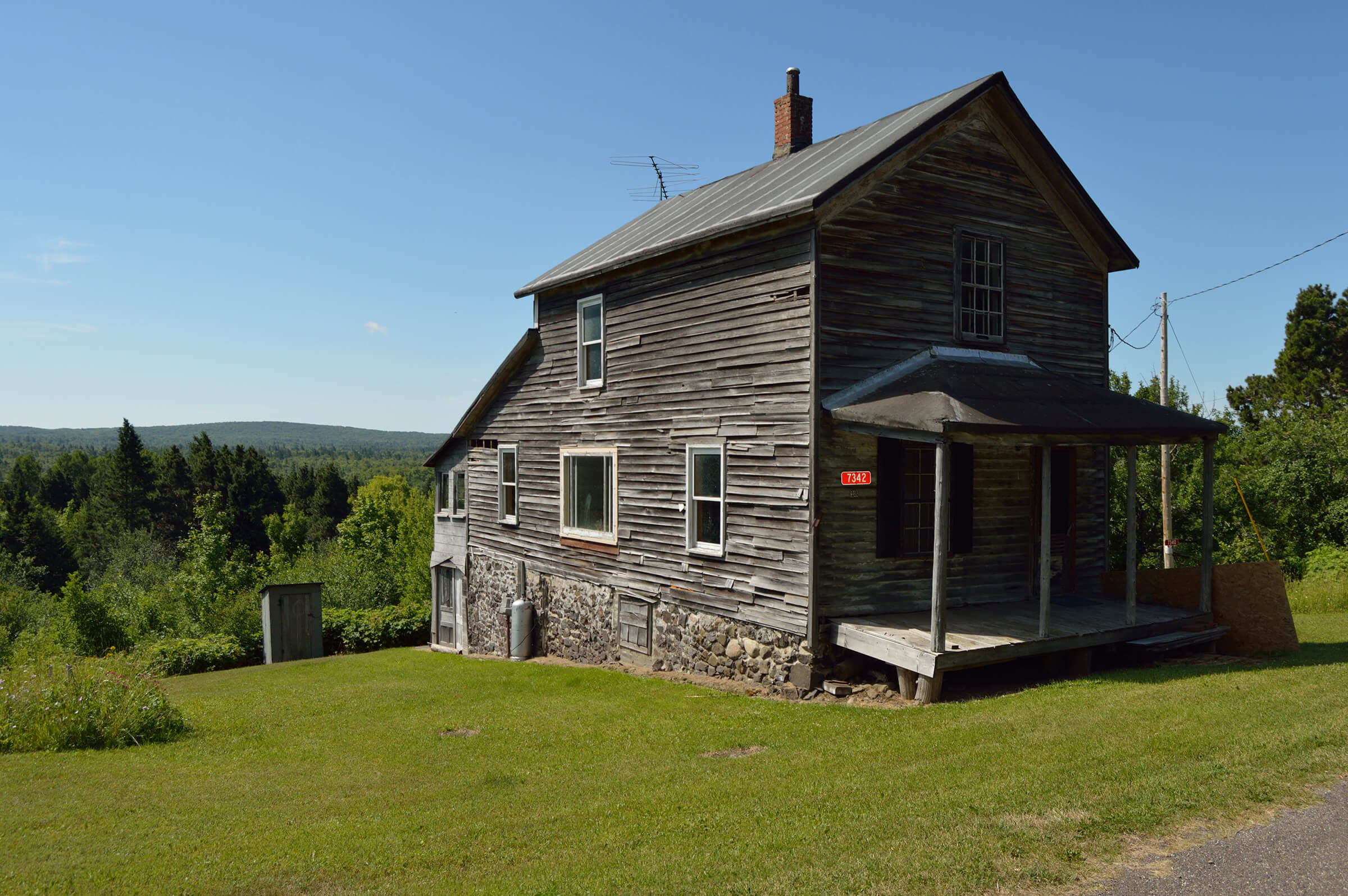 An old wooden house with a stone foundation, weathered siding, and a covered porch.