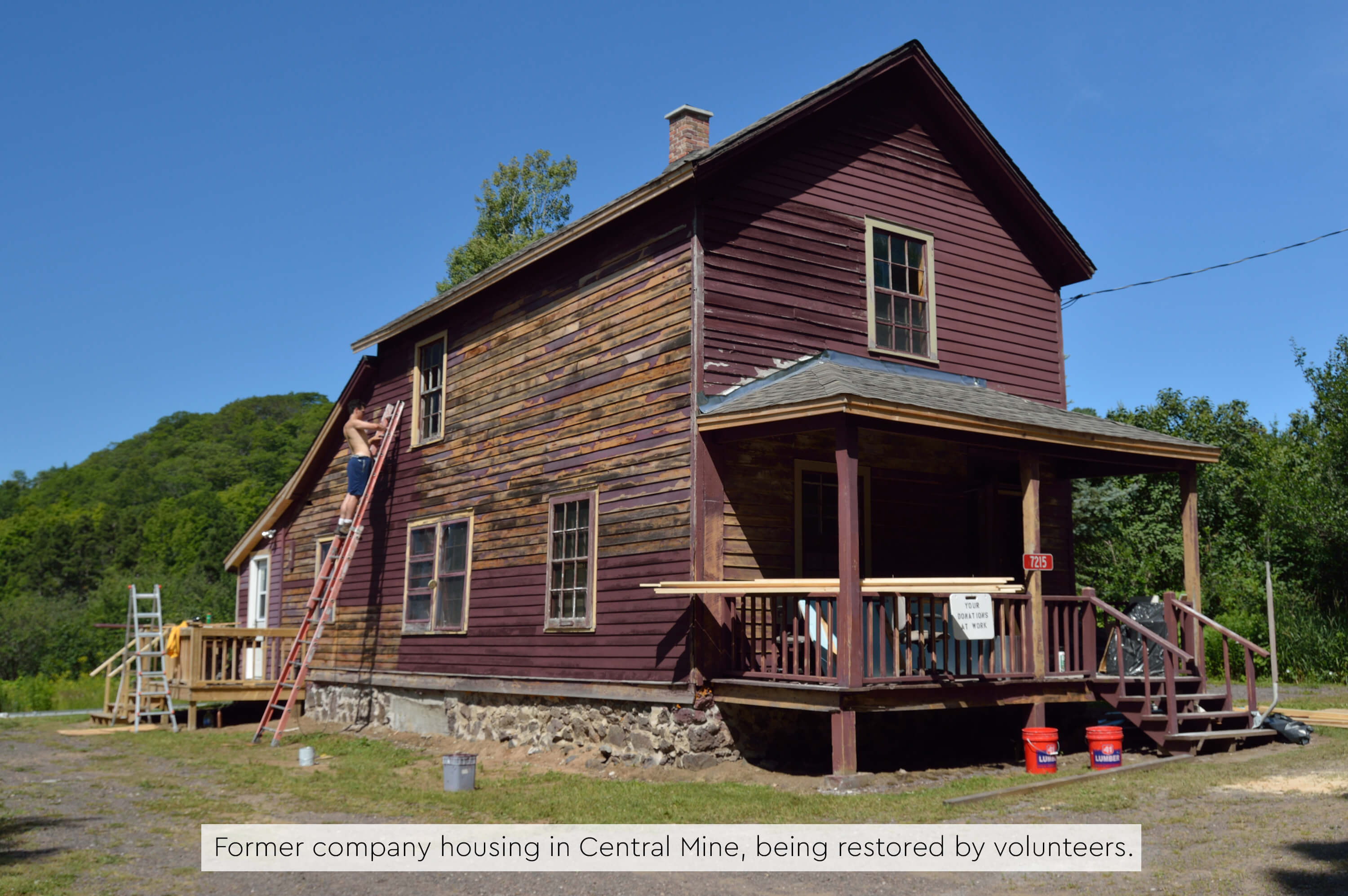 A wooden house with volunteers restoring the exterior siding.