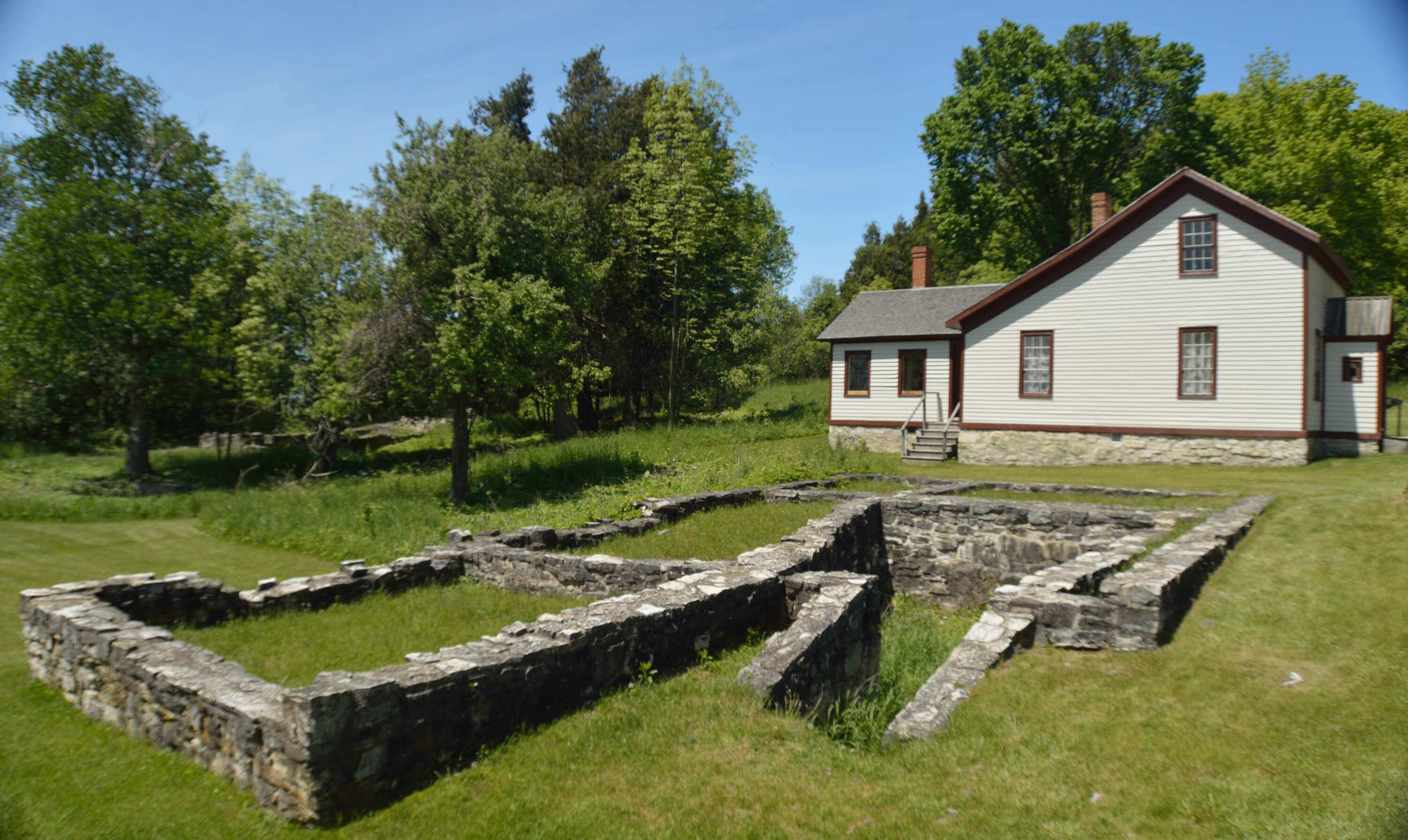 Ruins of a stone foundation in front of a restored white building in Fayette.