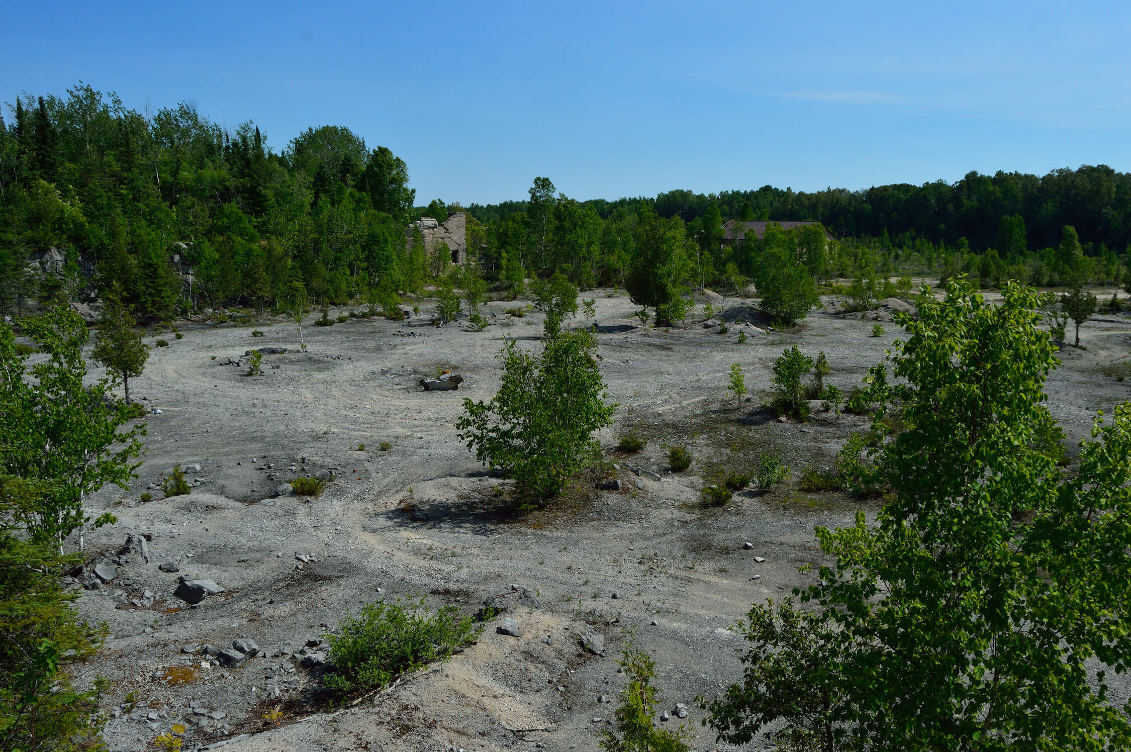 Open quarry landscape with sparse vegetation and remnants of structures.