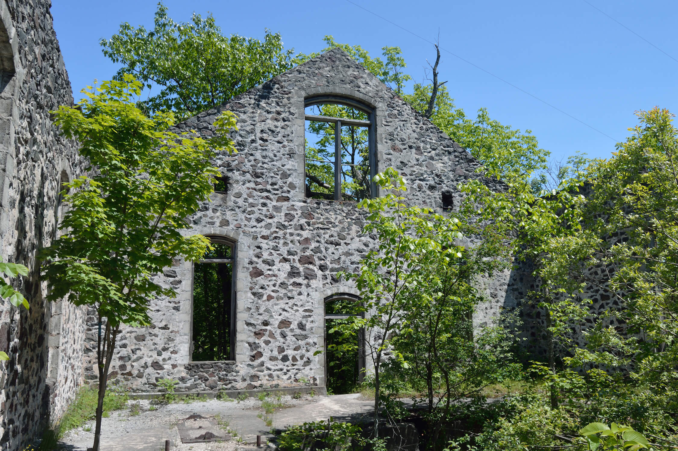 Ruins of a stone building with large empty windows, surrounded by trees and greenery.