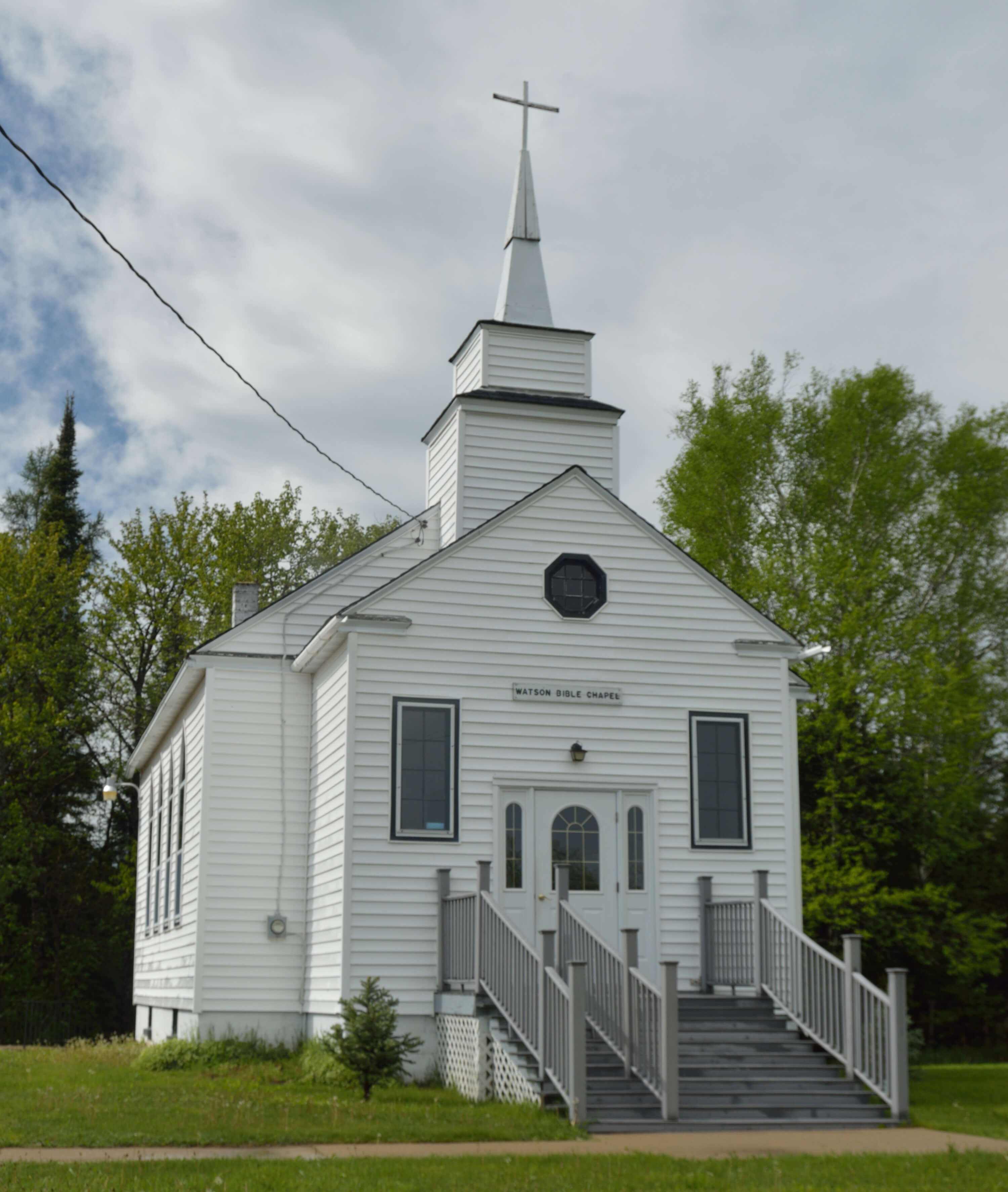 A small white church with a steeple and stairs leading to the entrance.