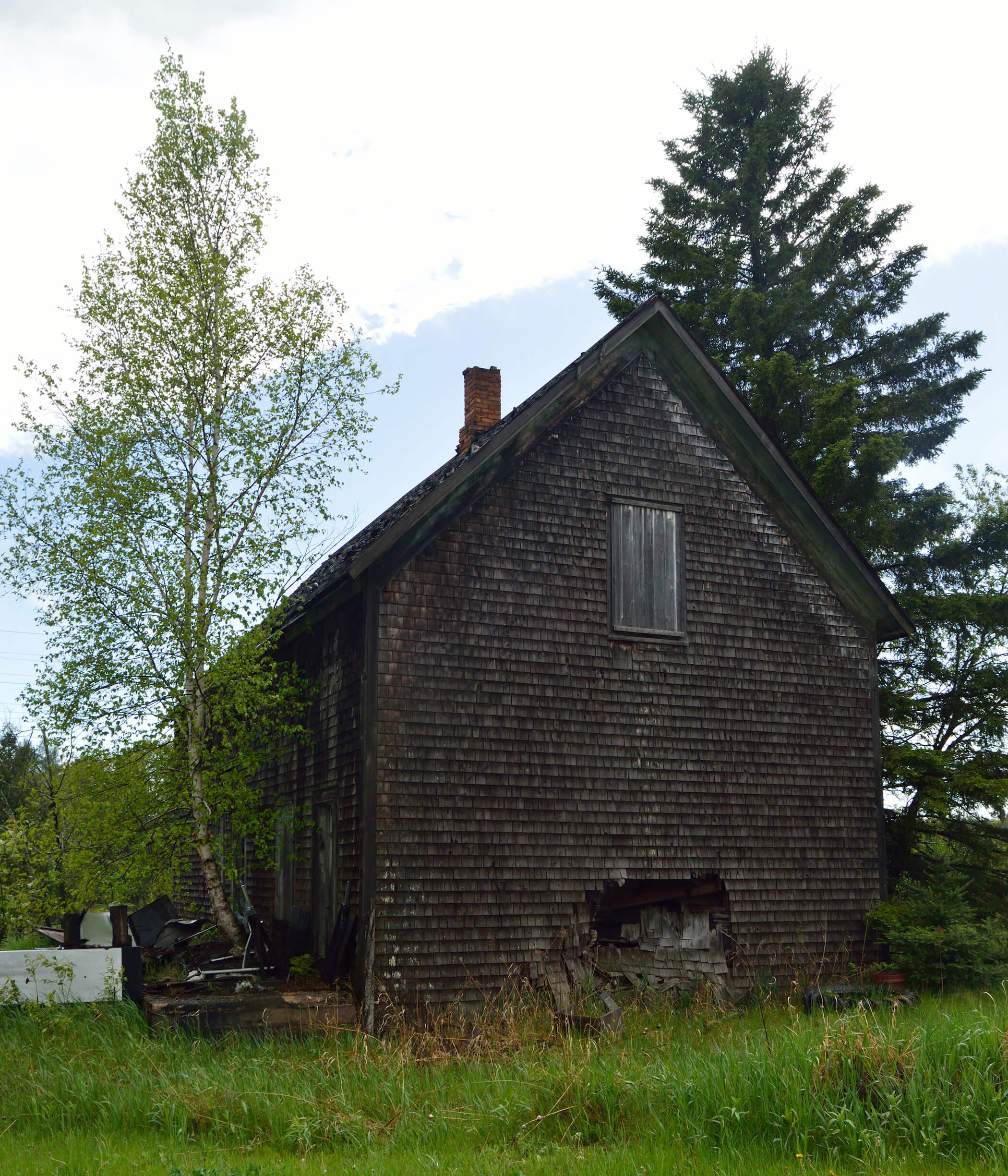 A deteriorating wooden house with missing shingles and a damaged foundation.