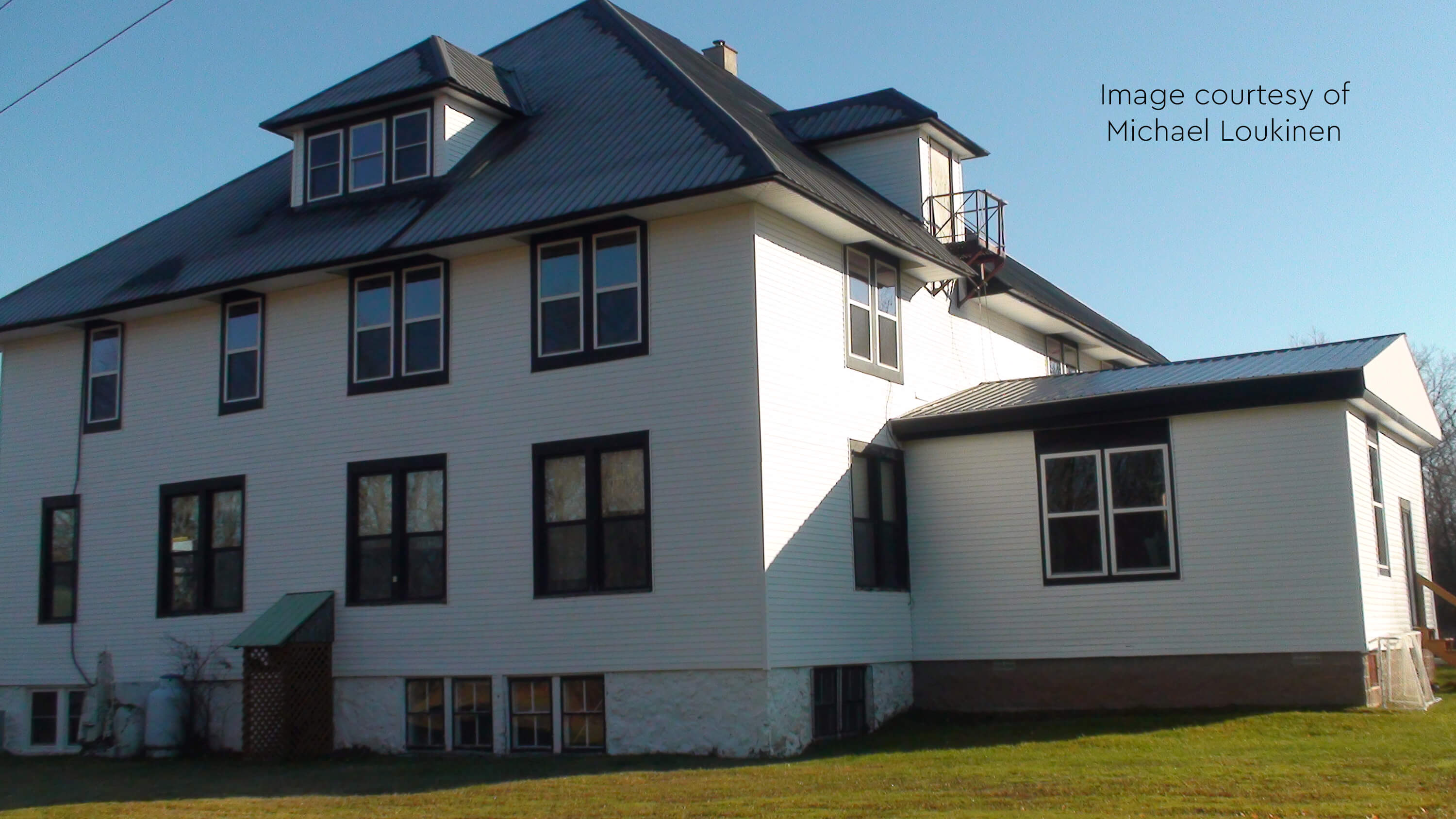 A large two-story white school building with a black roof and multiple windows.