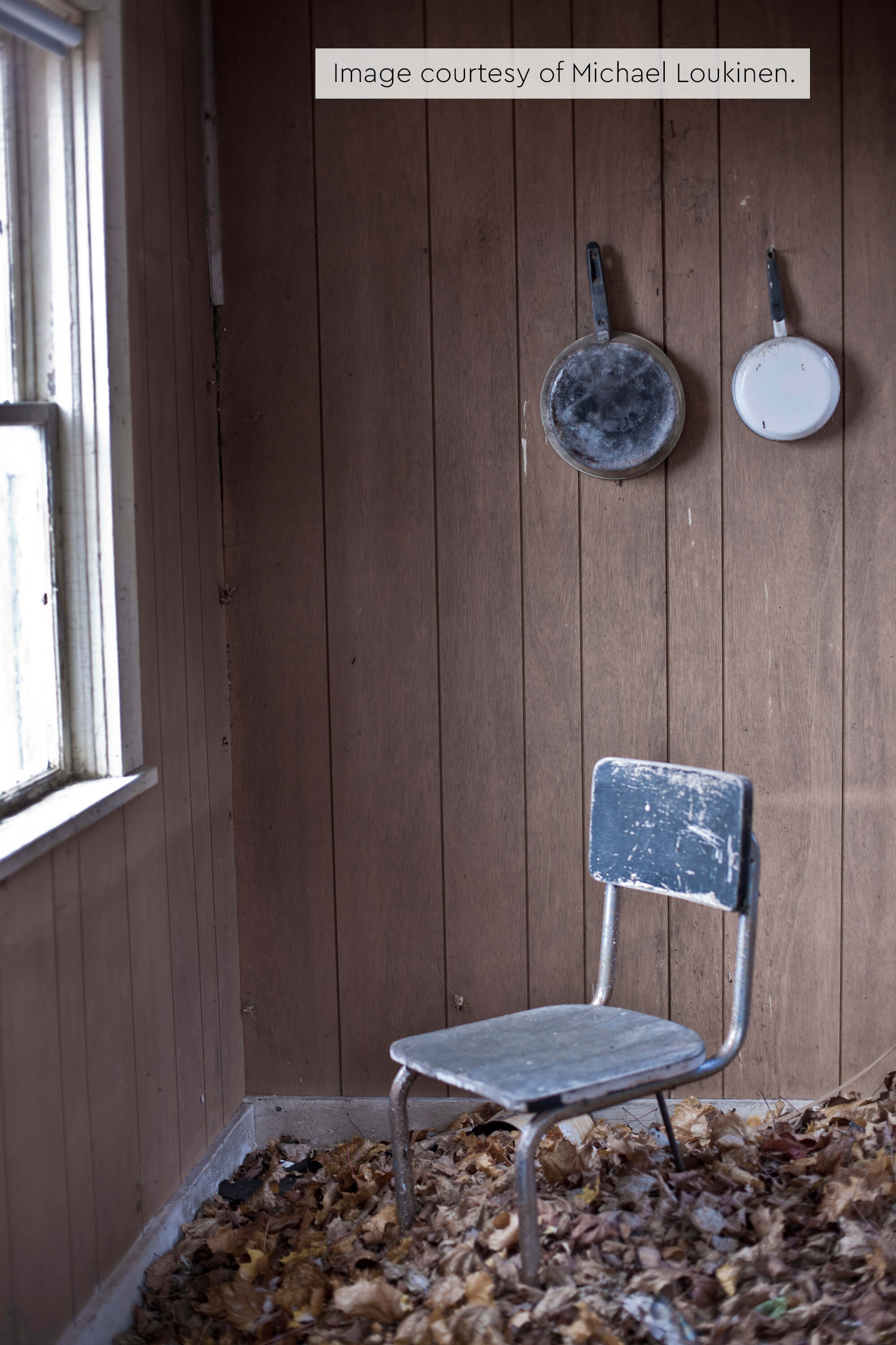 Dusty metal chair and old pans in an abandoned room with fallen leaves on the floor.