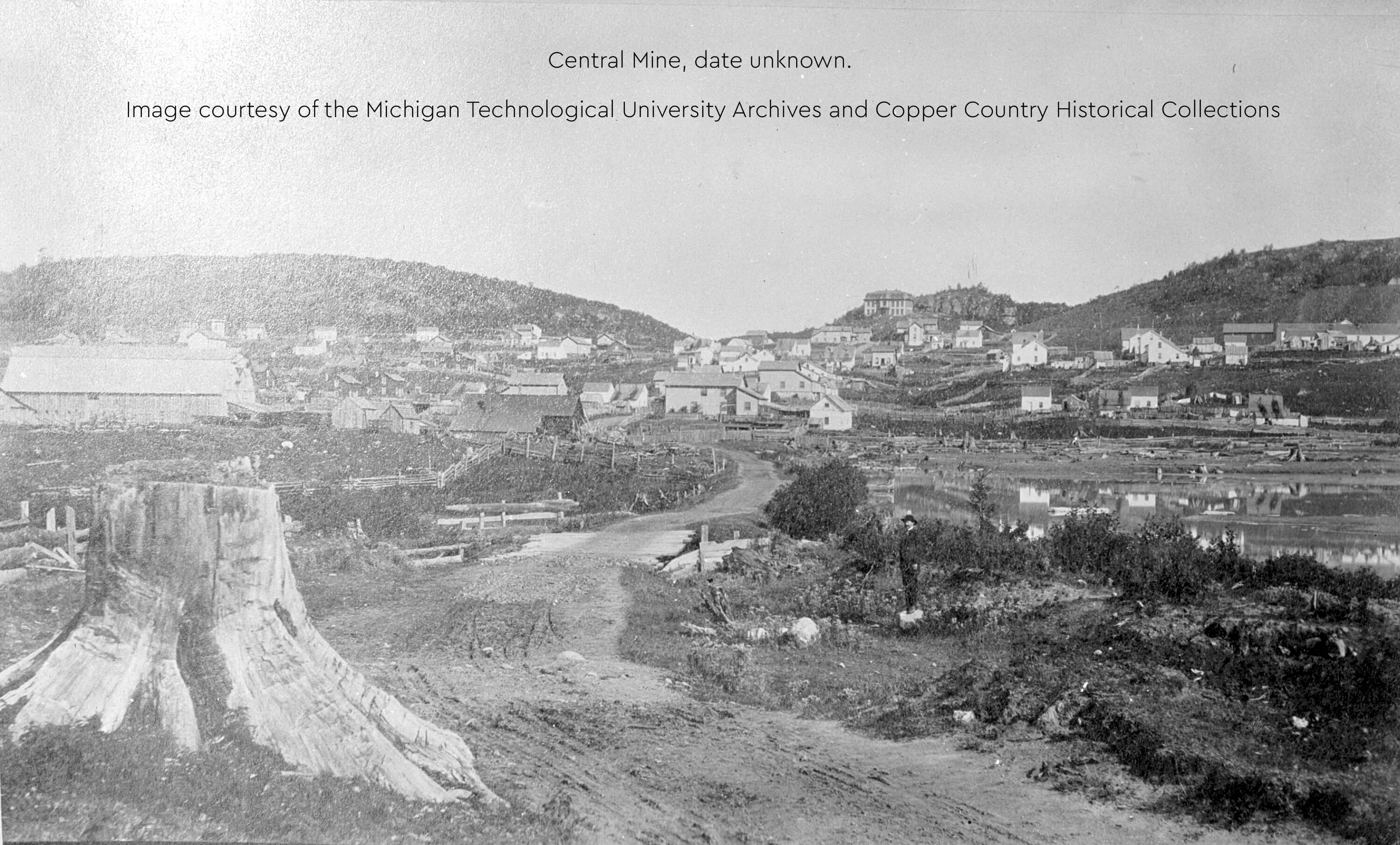 A historic view of Central Mine, showing buildings, hills, dirt roads, and a large tree stump.