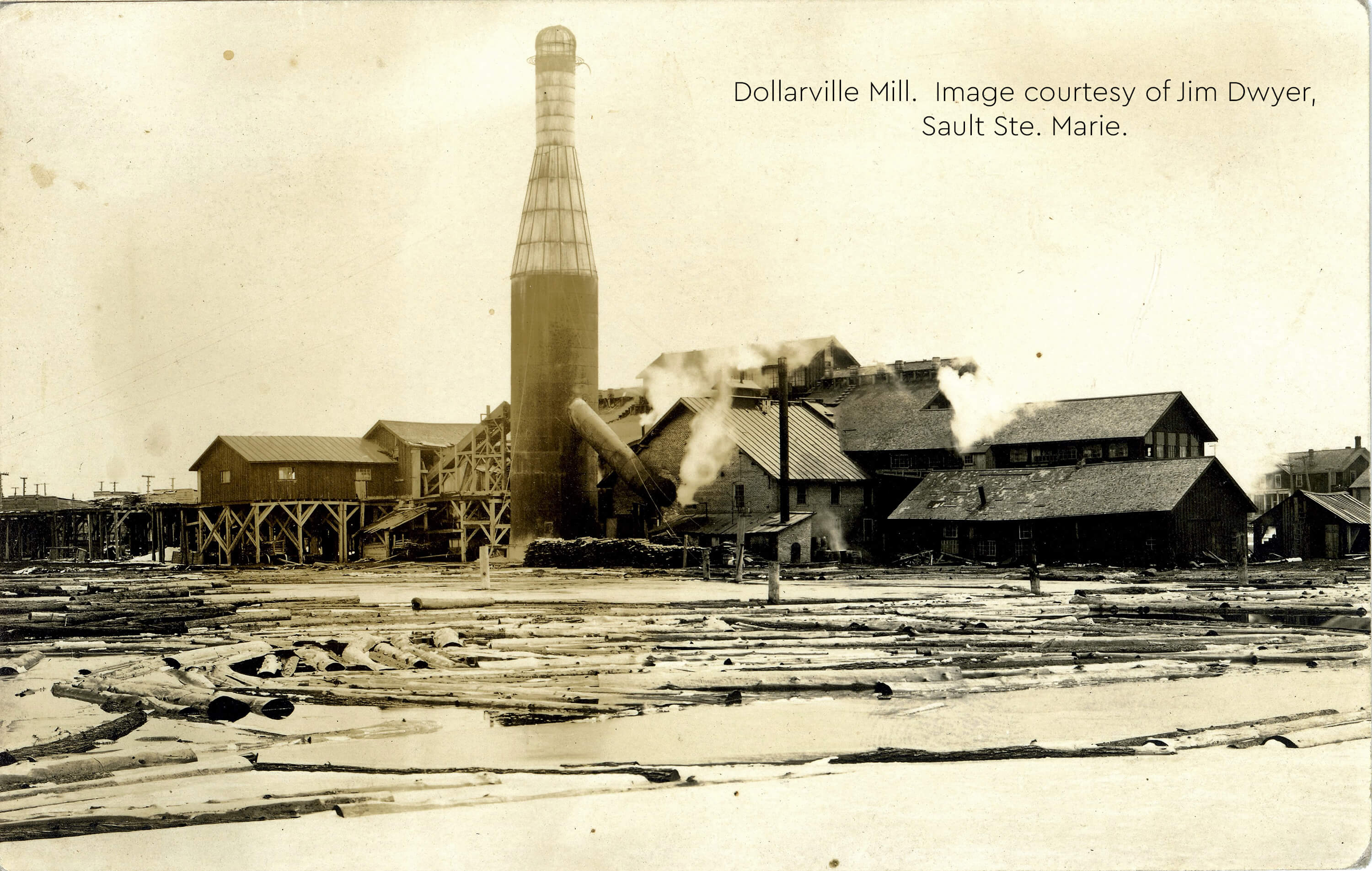 Historical photo of Dollarville sawmill with logs and smoke.
