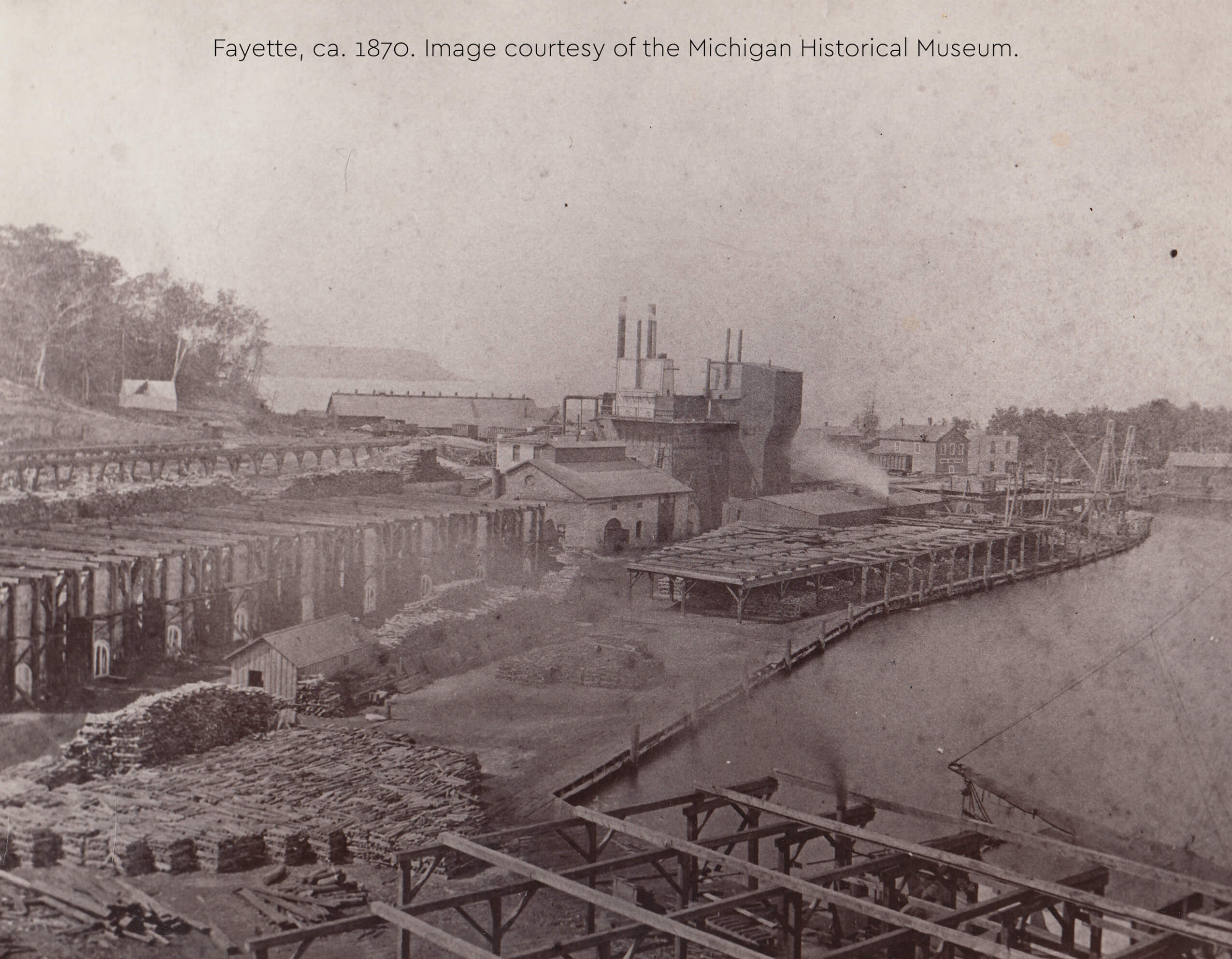 Historic photo of Fayette's harbor with furnaces, buildings, and lumber piles, ca. 1870.