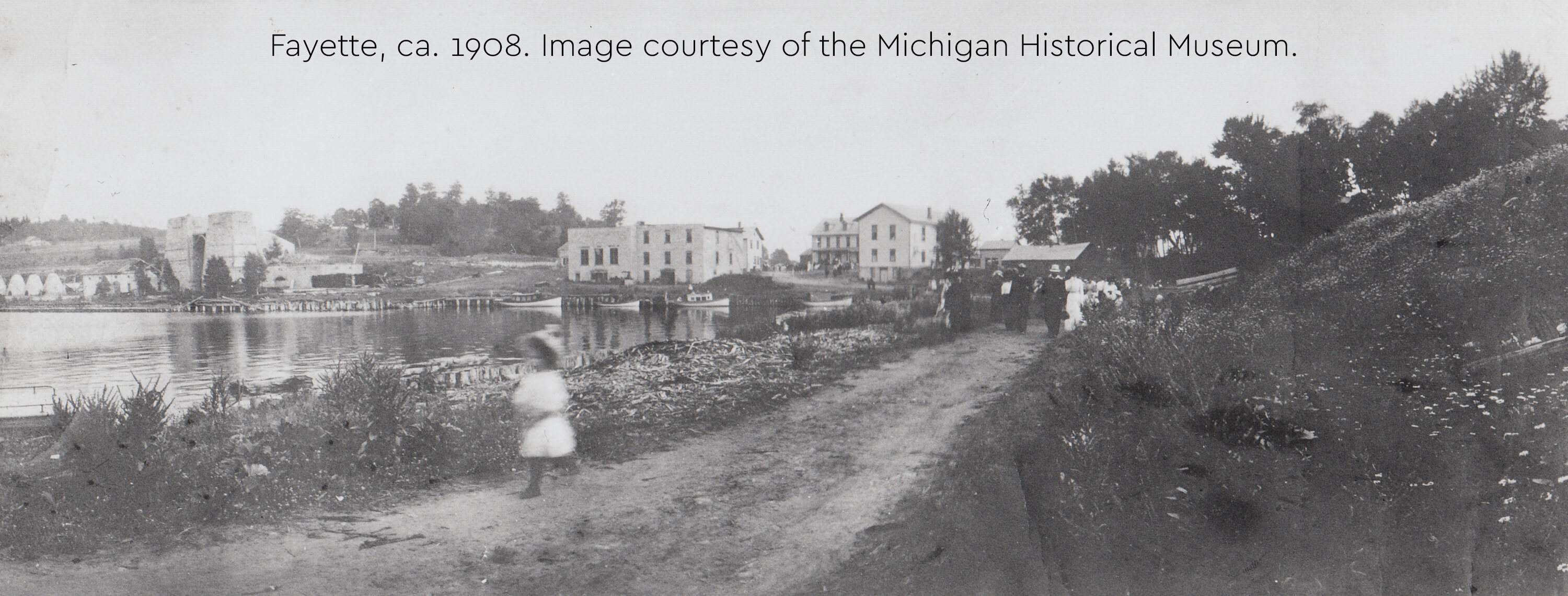 Historic photo of Fayette's harbor, stone ruins, and townspeople walking, ca. 1908.