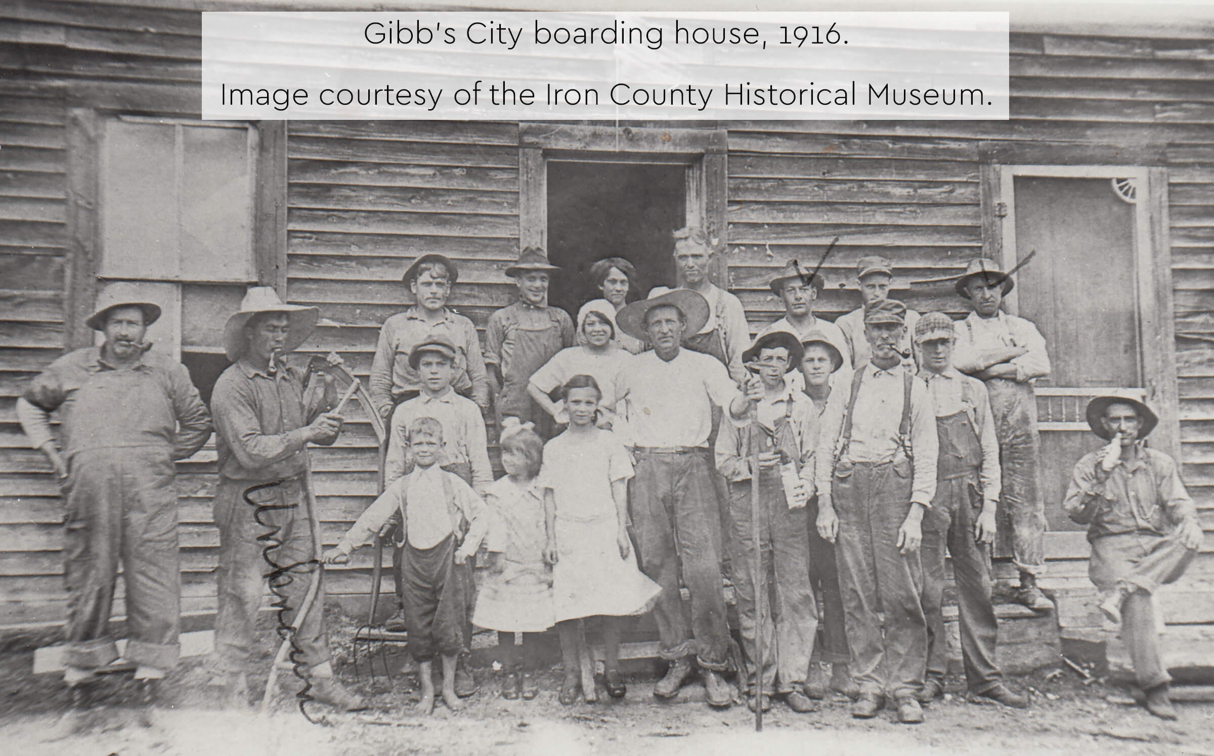A historic photograph of men, women, and children in front of a boarding house in 1916.