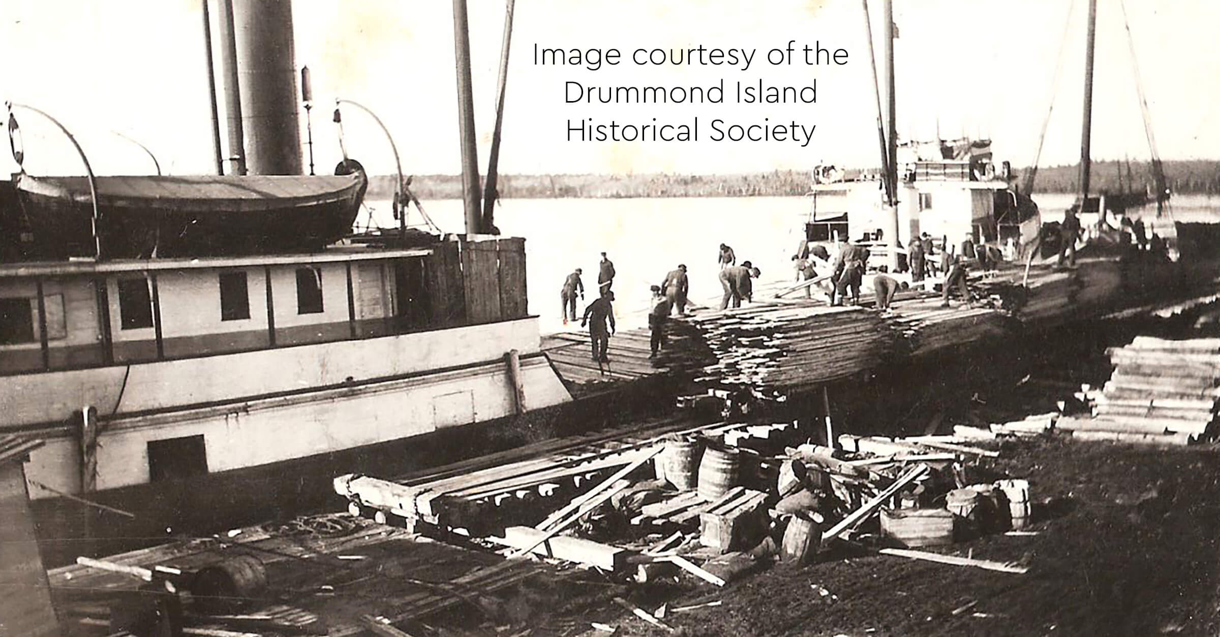 Historic image of workers loading lumber onto ships at a dock.