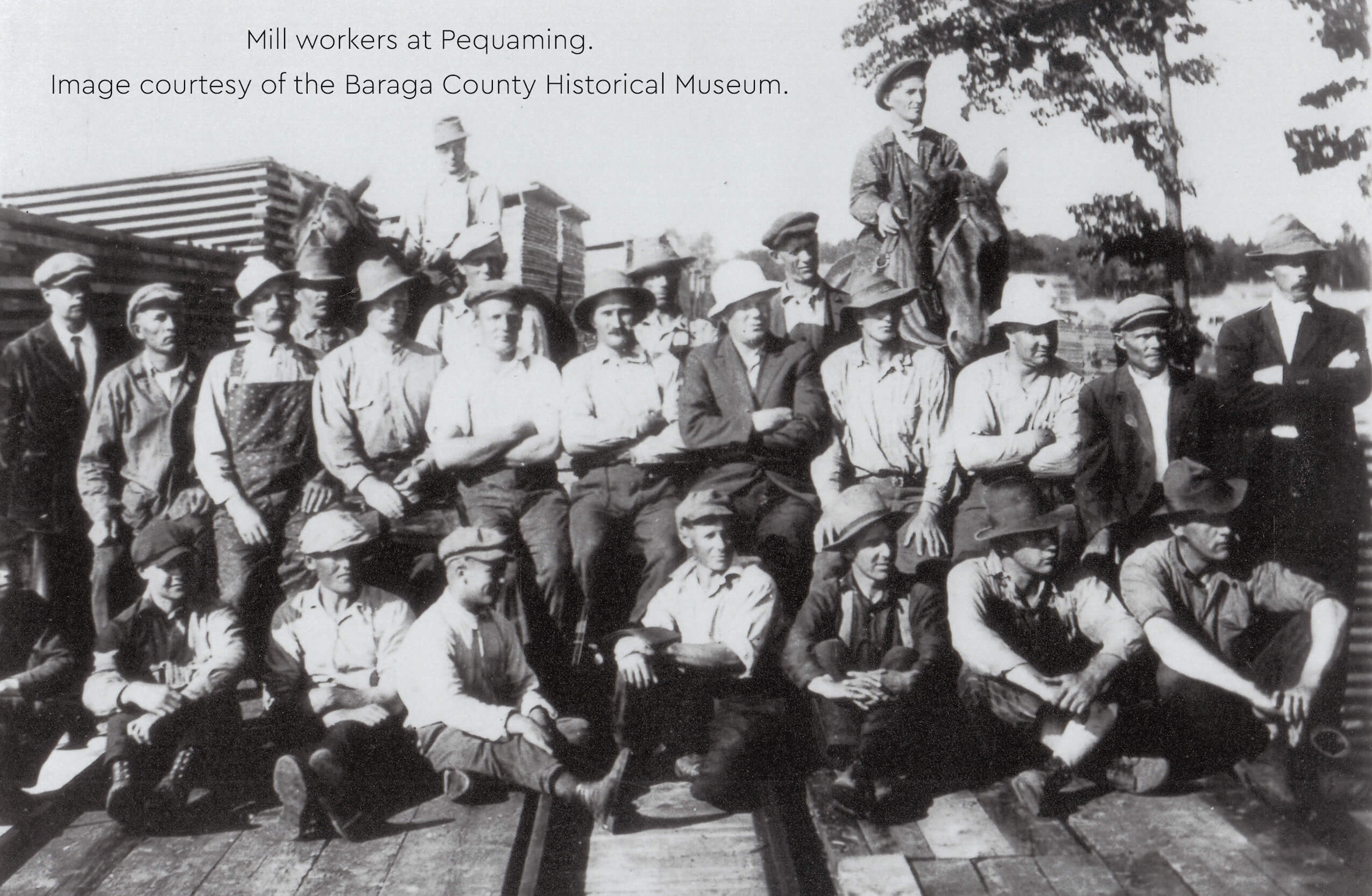 Historical image of mill workers in Pequaming posing on lumber stacks