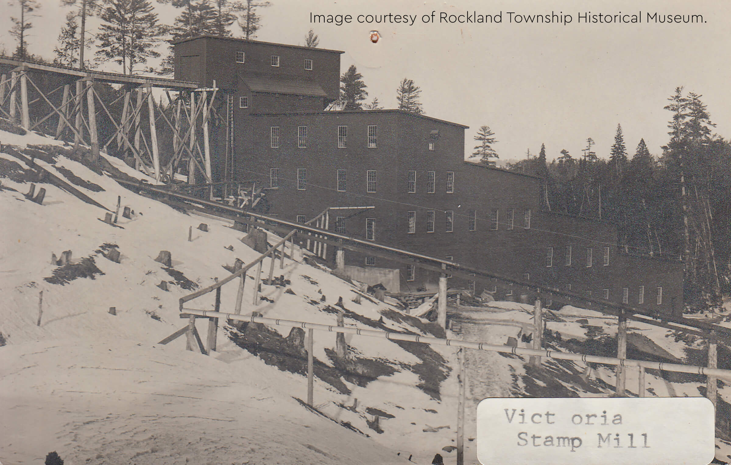 Historic photo of the Victoria Stamp Mill, a large multi-story wooden structure on a hillside.
