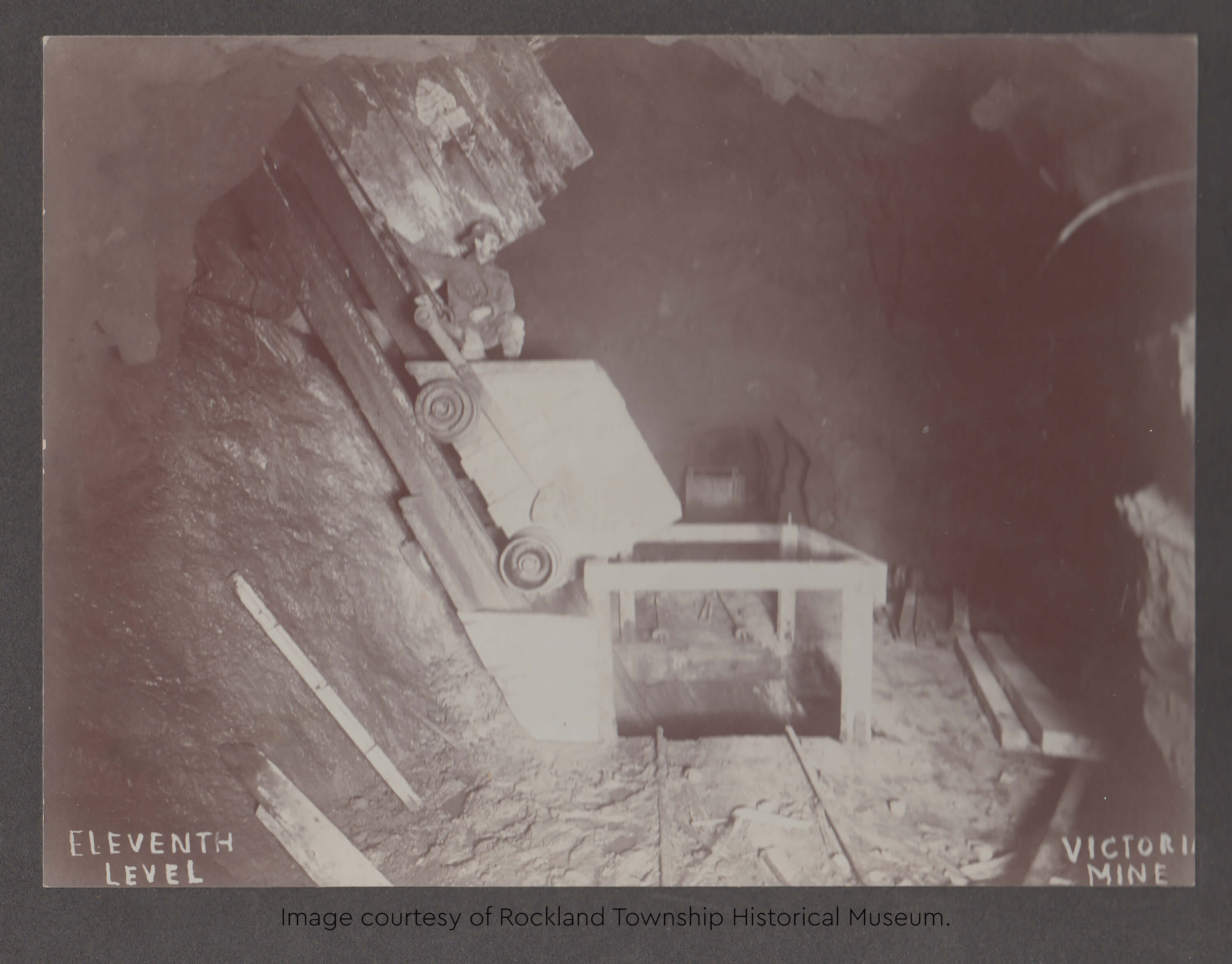 Historic photo of a miner sitting on an ore cart in the Victoria Mine's eleventh level.