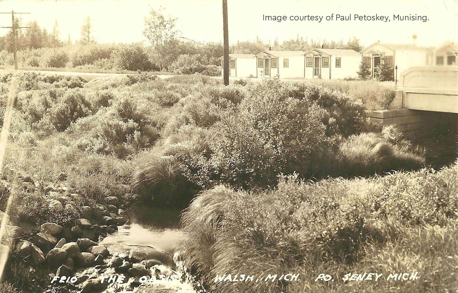 Historic 1938 image of The Oasis in Walsh, showing a creek and nearby buildings.