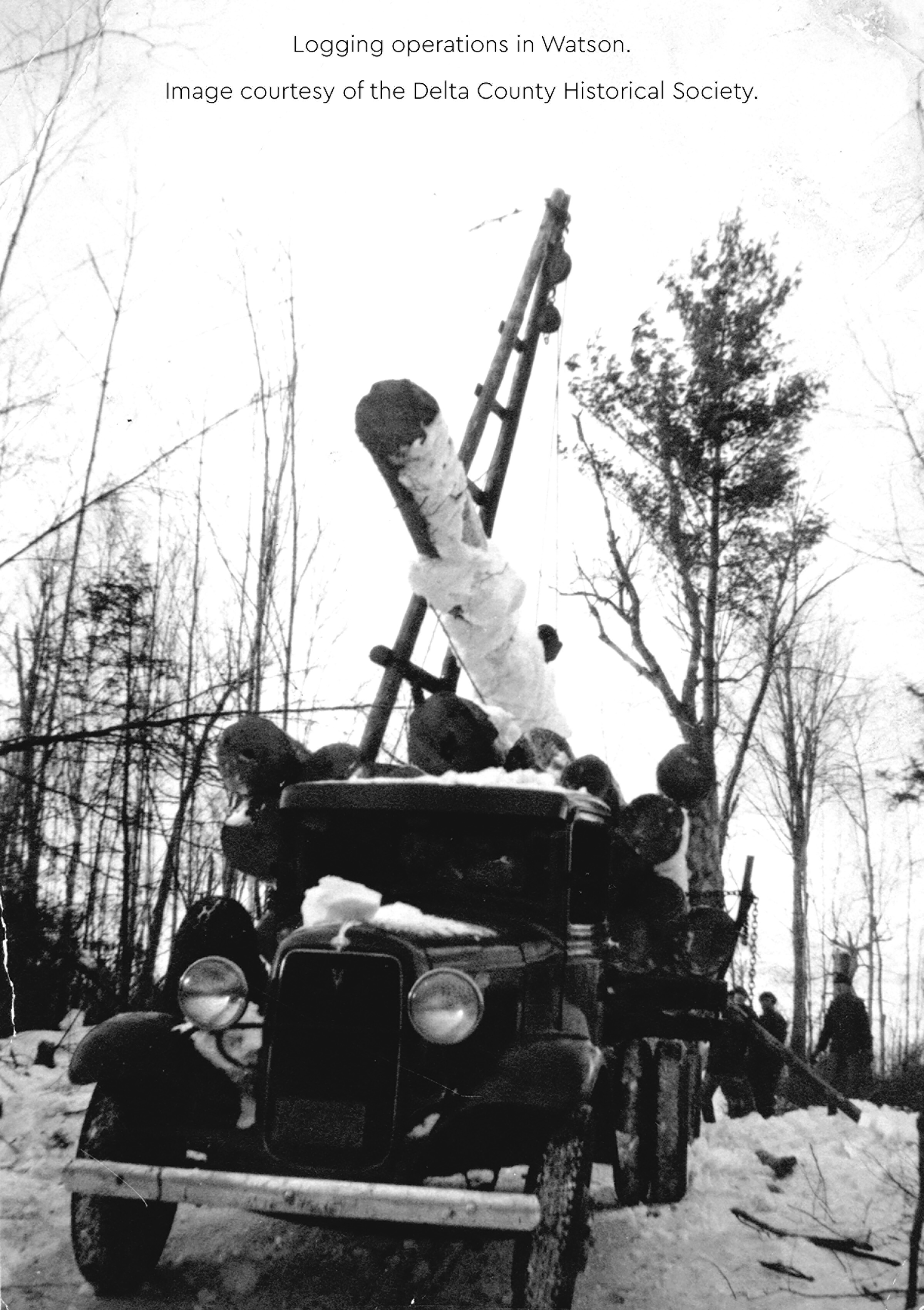 Historic logging truck with logs being lifted by an A-frame loader in winter.