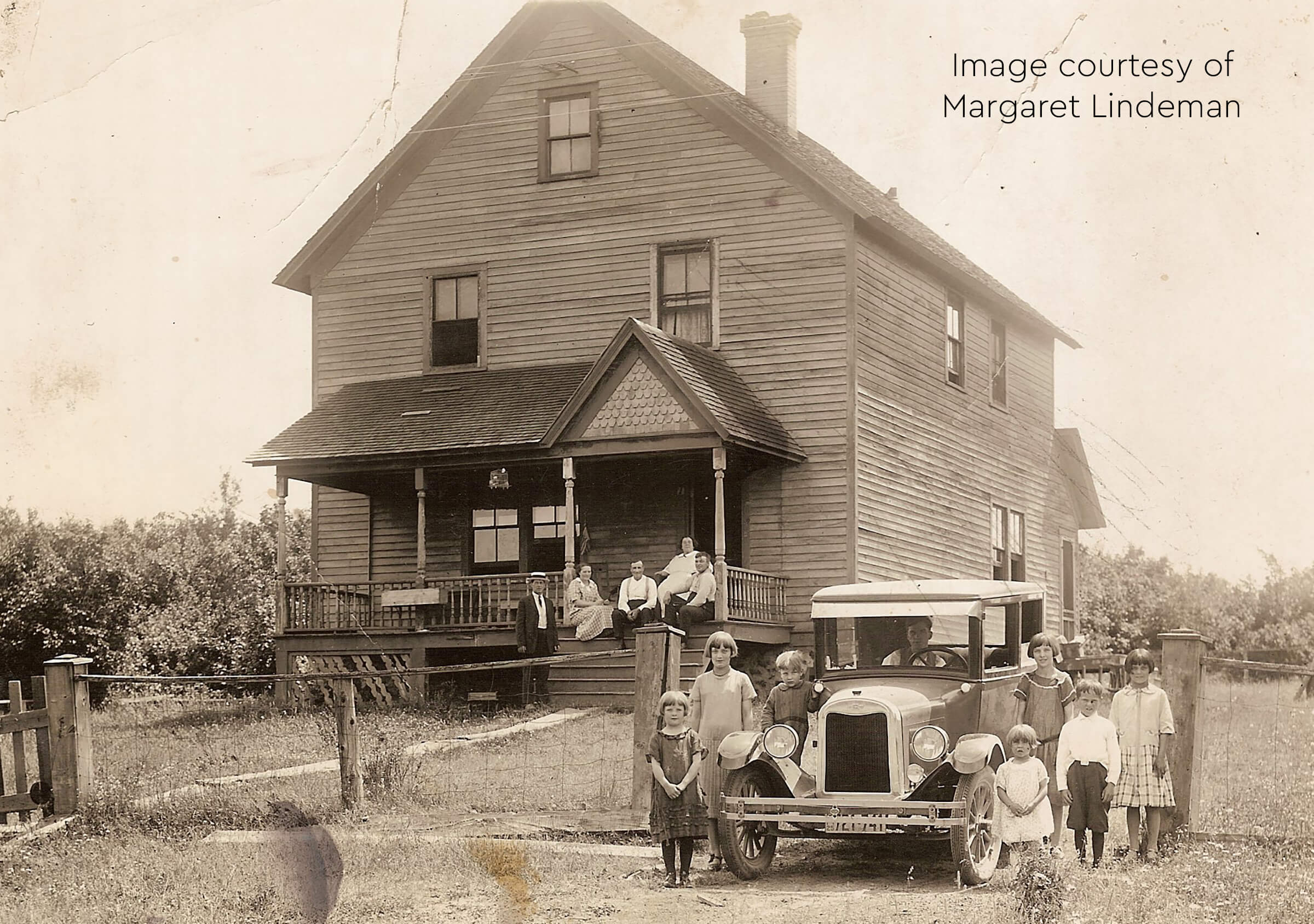 Historic photo of a family posing in front of a large wooden house with a vintage car.