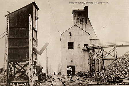 Historic photo of a mine shaft structure at the Winona Mine with conveyor and ore piles.