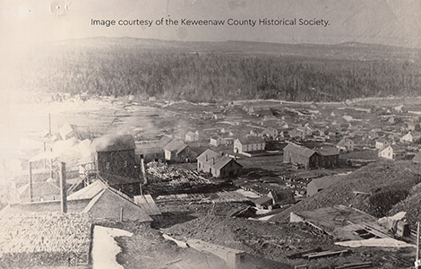 Historic photo of Central Mine showing wooden buildings, lumber stacks, and hills in the background.