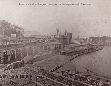 Historic photo of Fayette's harbor with furnaces, buildings, and lumber piles, ca. 1870.