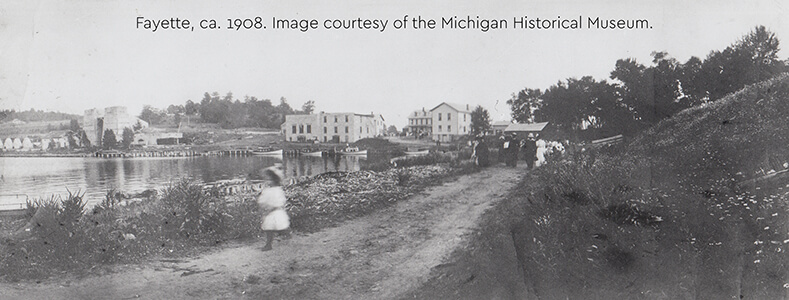 Historic photo of Fayette's harbor, stone ruins, and townspeople walking, ca. 1908.