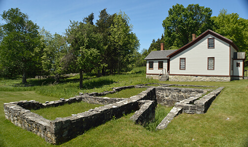 Ruins of a stone foundation in front of a restored white building in Fayette.