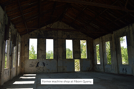 Interior of the former machine shop with empty walls and tall windows.
