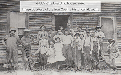 A historic photograph of men, women, and children in front of a boarding house in 1916.