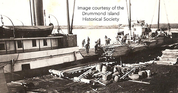 Historic image of workers loading lumber onto ships at a dock.