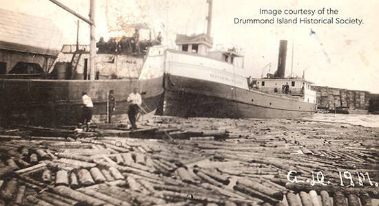 Historic image of logs being loaded onto the Matthew Wilson ship.