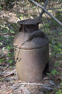 Old rusted milk can with broken handles, partially buried in forest debris in Tula, Michigan.