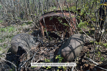 Rusting remains of an early automobile frame overgrown with brush in Tula, Michigan.