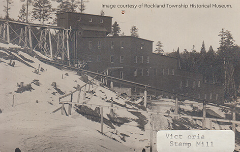 Historic photo of the Victoria Stamp Mill, a large multi-story wooden structure on a hillside.
