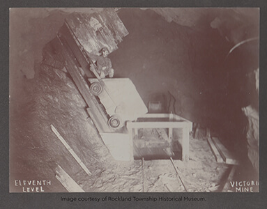 Historic photo of a miner sitting on an ore cart in the Victoria Mine's eleventh level.
