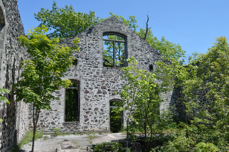 Ruins of a stone building with large empty windows, surrounded by trees and greenery.