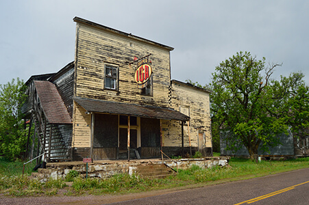 Abandoned wooden IGA store with faded paint and broken windows.