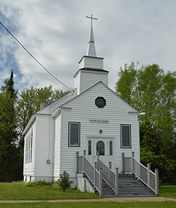 A small white church with a steeple and stairs leading to the entrance.