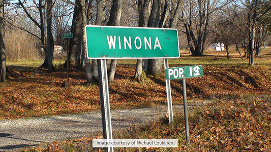 Green Winona town sign with population sign reading 13, set along a rural road.