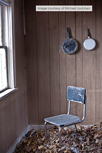 Dusty metal chair and old pans in an abandoned room with fallen leaves on the floor.