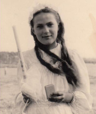 Helen in a white dress holding her first communion candle and prayer book.